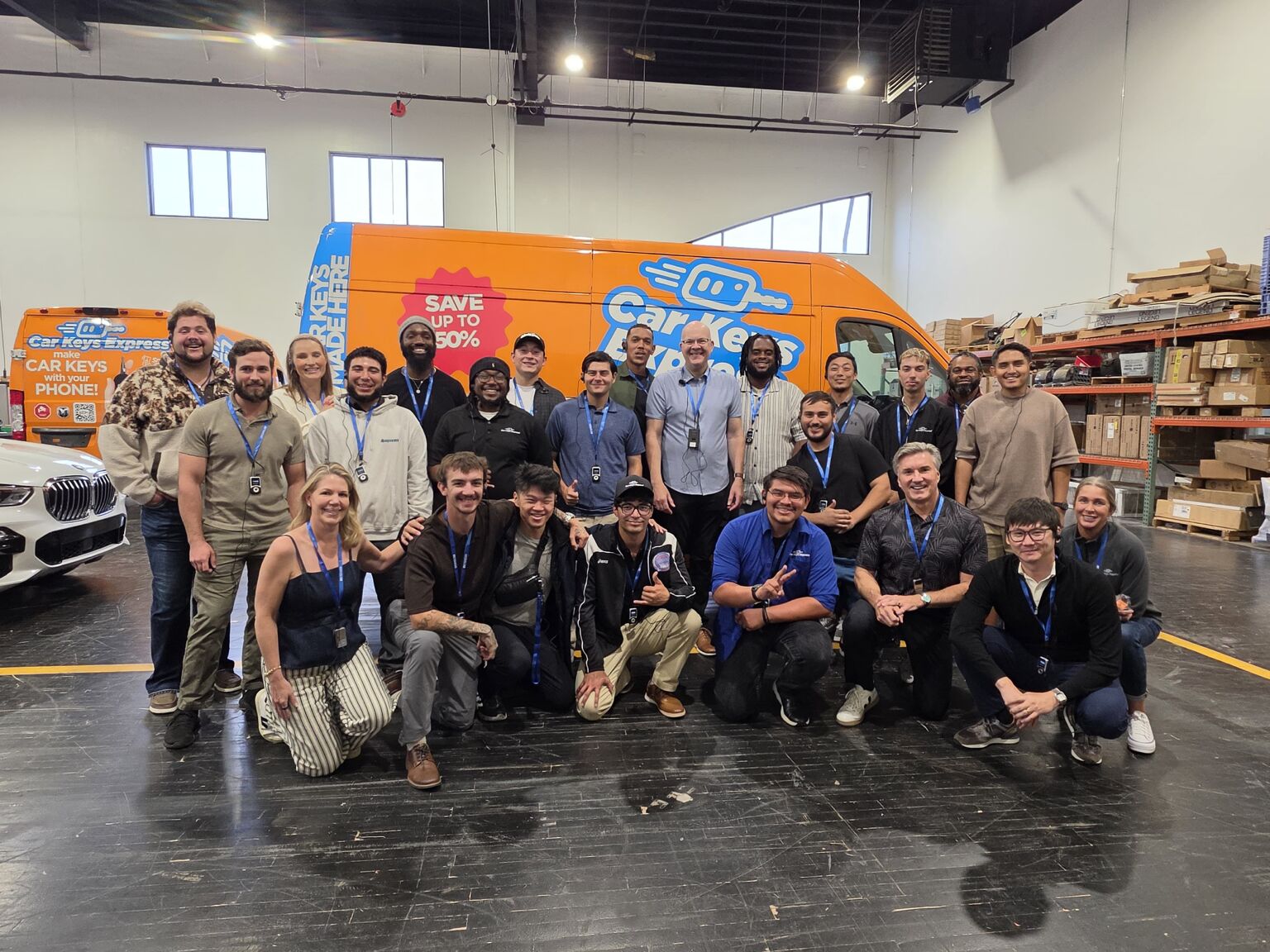 Peak Provisions team members wearing training lanyards, posed together in a Car Keys Express warehouse in front of an orange Car Keys Express service van